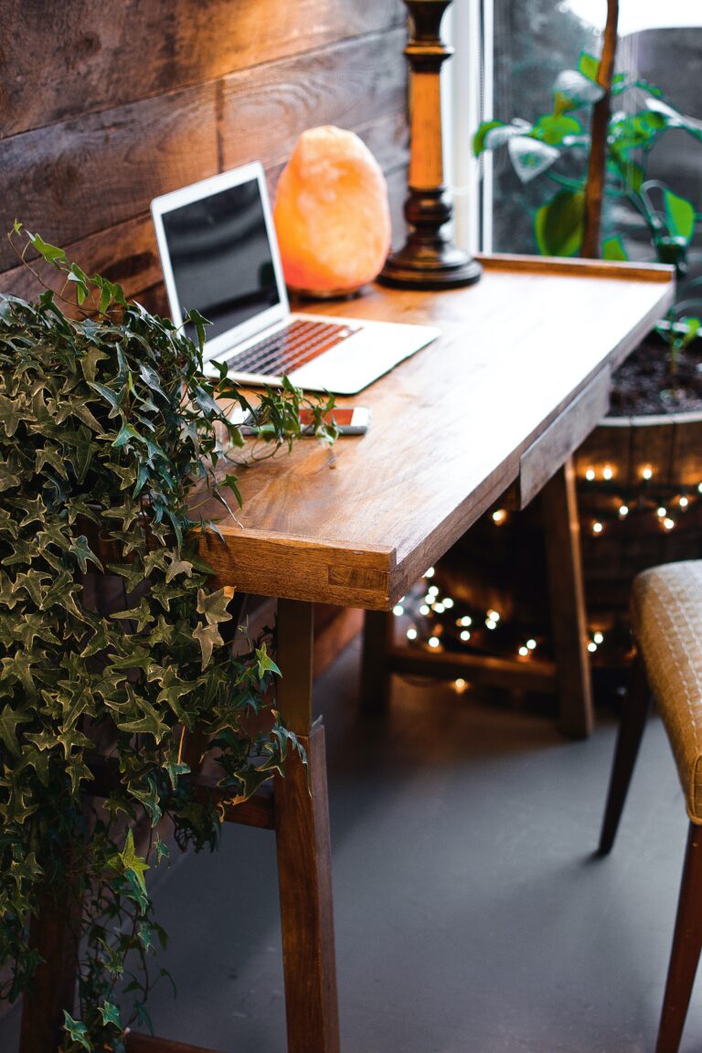 Laptop on wooden table surrounded by plants.